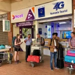 International travelers with luggage carts standing at the official Ncell and Nepal Telecom Namaste 4G tourist SIM card activation booths inside Tribhuvan International Airport arrivals terminal in Kathmandu.