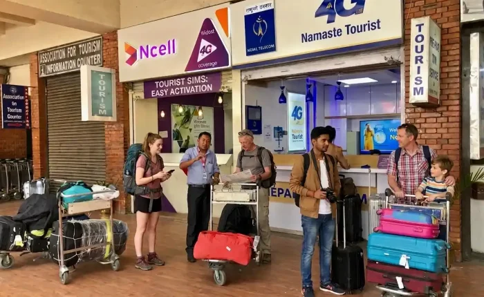 International travelers with luggage carts standing at the official Ncell and Nepal Telecom Namaste 4G tourist SIM card activation booths inside Tribhuvan International Airport arrivals terminal in Kathmandu.