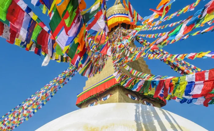 A vibrant low-angle shot of Boudhanath Stupa's golden peak surrounded by a canopy of multi-colored prayer flags against a blue sky