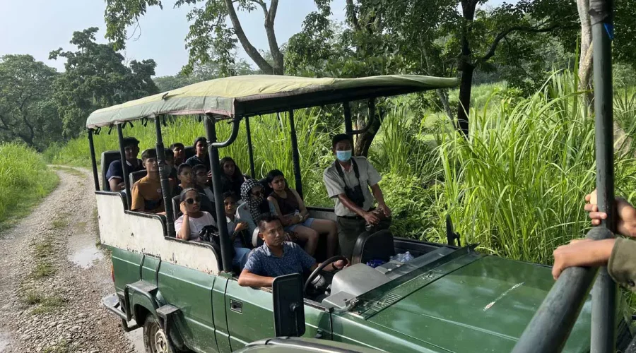 International travelers riding in an open-top green 4x4 safari jeep with a nature guide along a dirt trail in Chitwan National Park.