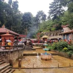 The flowing riverbed and water fountain feature at the bottom of the Dakshinkali Temple gorge, surrounded by traditional brick architecture.