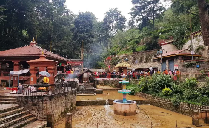 The flowing riverbed and water fountain feature at the bottom of the Dakshinkali Temple gorge, surrounded by traditional brick architecture.