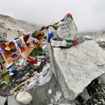The iconic graffiti-painted stone marker at Everest Base Camp pointing to 5364m surrounded by colorful Buddhist prayer flags.