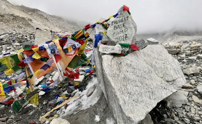 The iconic graffiti-painted stone marker at Everest Base Camp pointing to 5364m surrounded by colorful Buddhist prayer flags.