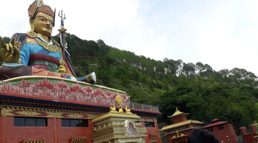 The colossal, brightly colored Guru Padmasambhava (Guru Rinpoche) statue on a lotus throne against a forested hill canopy in Pharping