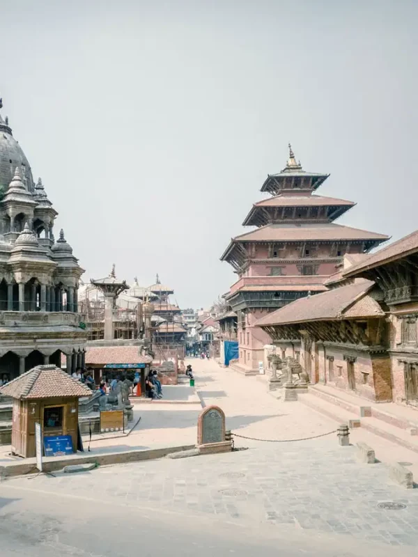 An side-angle view of the historic stone Krishna Mandir and the red brick palace complex buildings in Patan Durbar Square.