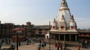The historic white Shikhara-style Machindranath Temple (Bungadyo) standing in the open brick courtyard of Bungmati village with locals gathering.