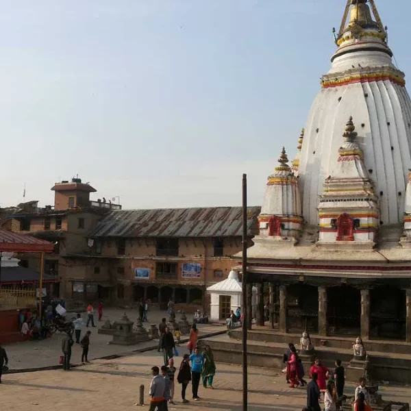 The historic white Shikhara-style Machindranath Temple (Bungadyo) standing in the open brick courtyard of Bungmati village with locals gathering.