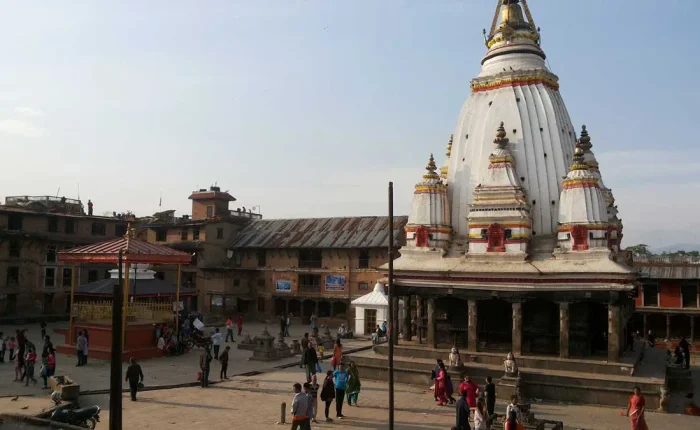 The historic white Shikhara-style Machindranath Temple (Bungadyo) standing in the open brick courtyard of Bungmati village with locals gathering.