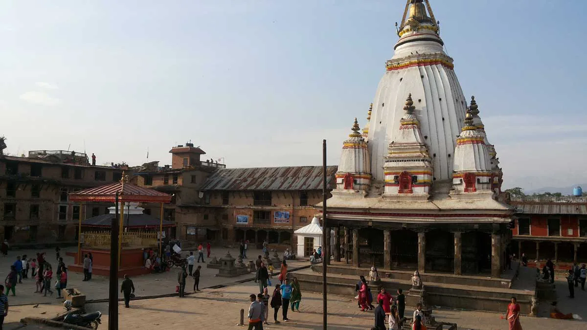 The historic white Shikhara-style Machindranath Temple (Bungadyo) standing in the open brick courtyard of Bungmati village with locals gathering.