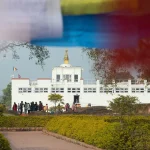 Tourists walking along a path toward the white Maya Devi Temple, the birthplace of Lord Buddha, framed by prayer flags.