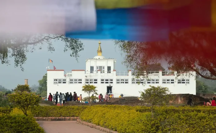 Tourists walking along a path toward the white Maya Devi Temple, the birthplace of Lord Buddha, framed by prayer flags.