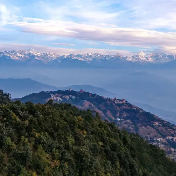 Panoramic view from a Nagarkot hilltop featuring the Nepal national flag waving on a ridge overlooking rolling hills and a massive snow-covered mountain range.