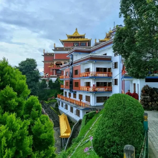 Modern white and red multi-story guest accommodations inside the Namo Buddha monastery complex, surrounded by manicured green bushes