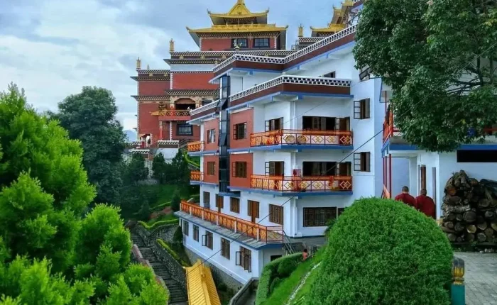 Modern white and red multi-story guest accommodations inside the Namo Buddha monastery complex, surrounded by manicured green bushes