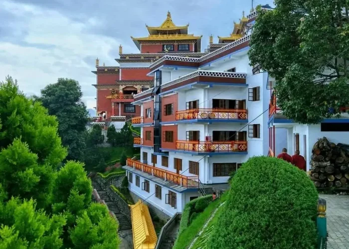 Modern white and red multi-story guest accommodations inside the Namo Buddha monastery complex, surrounded by manicured green bushes