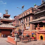 The historical three-tiered Narayan Temple courtyard in Dhulikhel old town, featuring red brick architecture and gold accents under a clear sky.