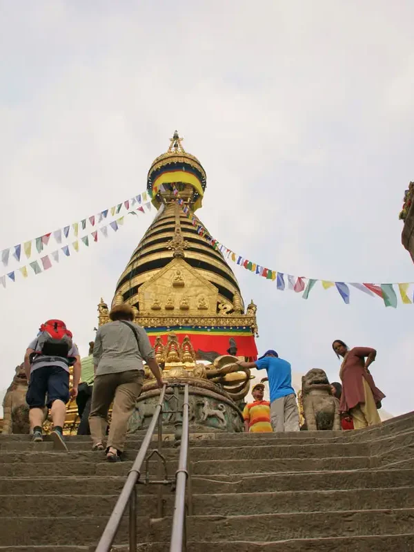 Tourists and travelers climbing the stone stairs leading up to the golden Swayambhunath Stupa in Kathmandu.