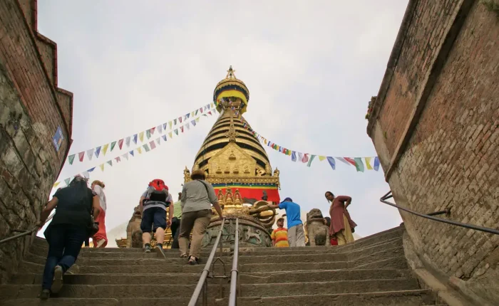 Tourists and travelers climbing the stone stairs leading up to the golden Swayambhunath Stupa in Kathmandu.