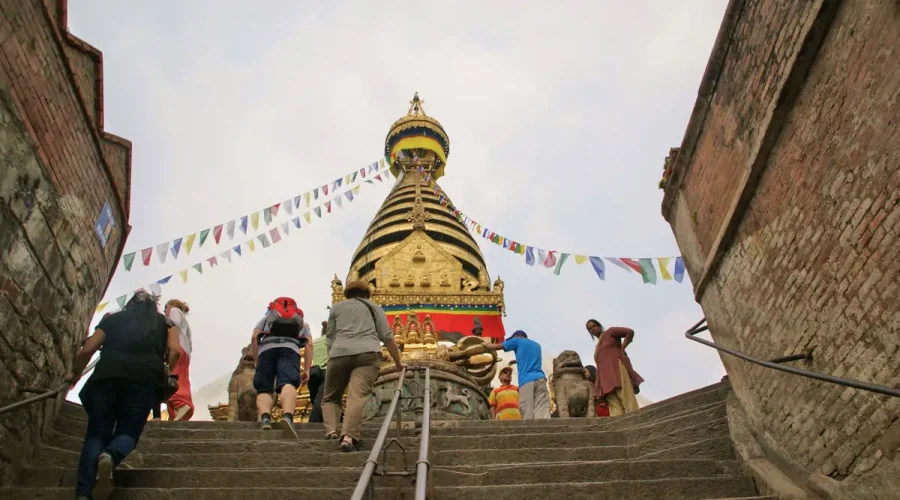 Tourists and travelers climbing the stone stairs leading up to the golden Swayambhunath Stupa in Kathmandu.
