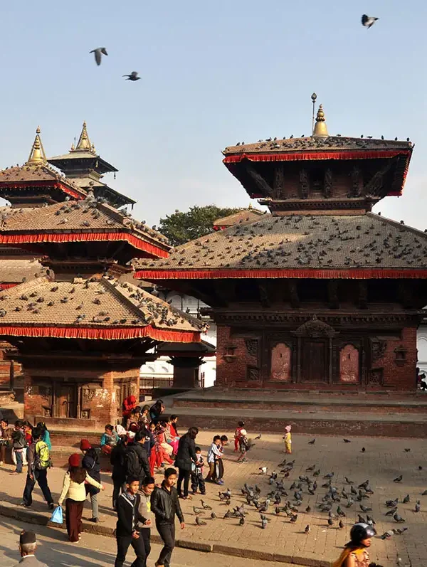 Tourists and pigeons gathered around the historic pagoda temples and the Garuda pillar at Kathmandu Durbar Square.