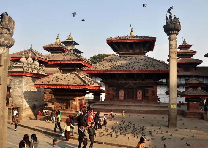 Tourists and pigeons gathered around the historic pagoda temples and the Garuda pillar at Kathmandu Durbar Square.