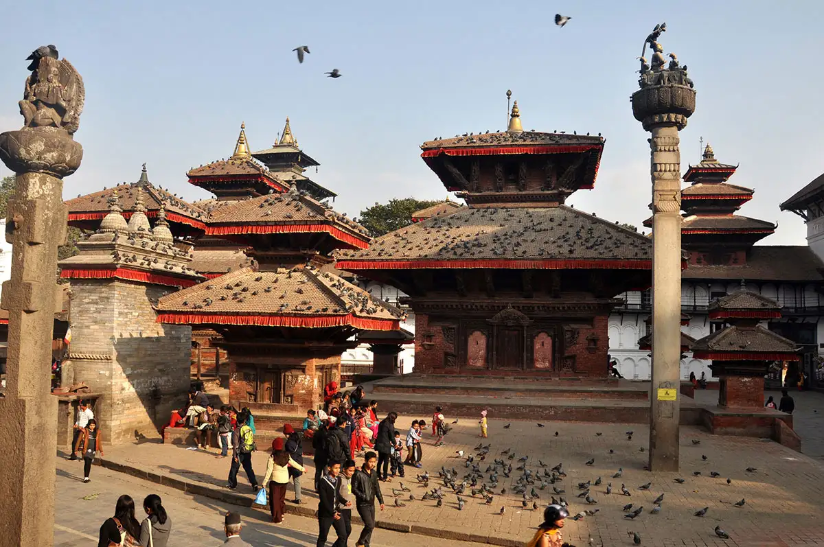 Tourists and pigeons gathered around the historic pagoda temples and the Garuda pillar at Kathmandu Durbar Square.