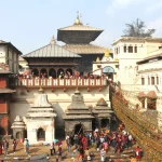A vibrant crowd gathered near the white stone stupas at Pashupatinath adorned with colorful string decorations.