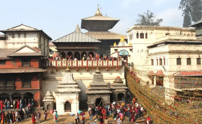 A vibrant crowd gathered near the white stone stupas at Pashupatinath adorned with colorful string decorations.