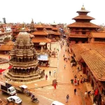 An elevated high-angle view looking down at the stone Krishna Mandir temple and red-tiled pagoda roofs of Patan Durbar Square.
