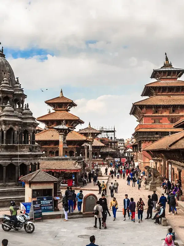 A lively daytime view of Patan Durbar Square showing the multi-tiered stone Krishna Mandir temple with visitors walking around.