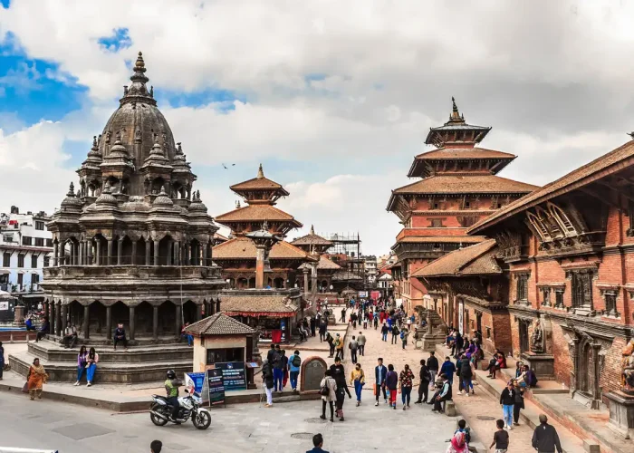 A lively daytime view of Patan Durbar Square showing the multi-tiered stone Krishna Mandir temple with visitors walking around.
