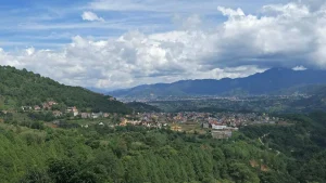 A sweeping panoramic landscape view of the hills, monastic towns, and valley settlements of Pharping under a dramatic cloudy blue sky.