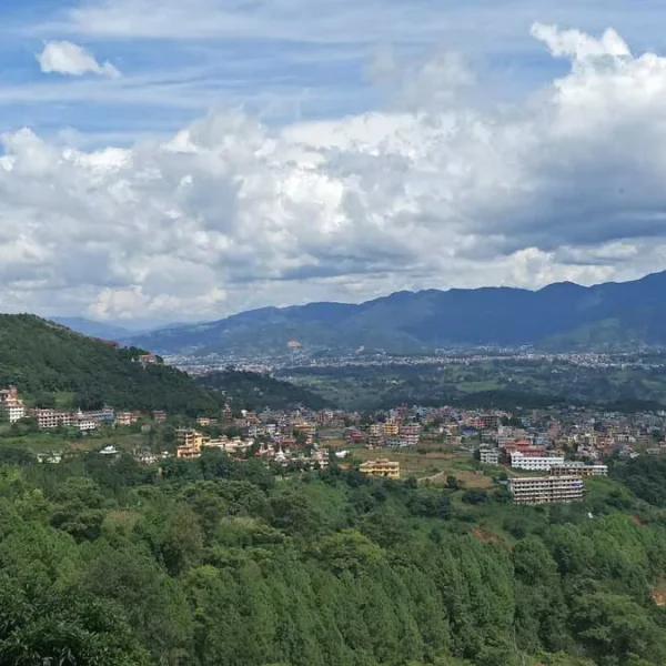 A sweeping panoramic landscape view of the hills, monastic towns, and valley settlements of Pharping under a dramatic cloudy blue sky.