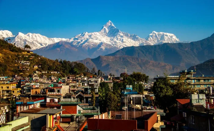 The colorful buildings of Pokhara city valley stretching towards the snow-covered peak of Mount Machapuchare under a clear blue sky.