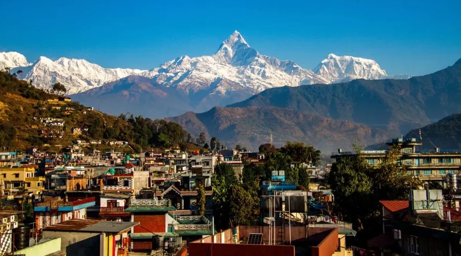 The colorful buildings of Pokhara city valley stretching towards the snow-covered peak of Mount Machapuchare under a clear blue sky.