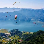 Multiple colorful paragliders soaring high over the lush green hills and blue waters of Phewa Lake, a popular adventure activity in Pokhara.