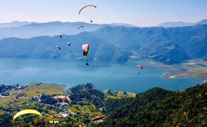 Multiple colorful paragliders soaring high over the lush green hills and blue waters of Phewa Lake, a popular adventure activity in Pokhara.