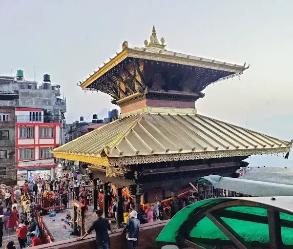 The historic two-tiered golden roof of the sacred Manakamana Devi Temple with crowds of devotees gathering in the courtyard.
