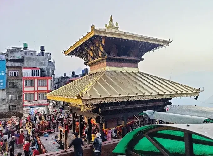 The historic two-tiered golden roof of the sacred Manakamana Devi Temple with crowds of devotees gathering in the courtyard.