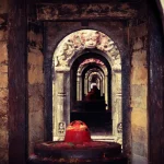 A symmetrical internal view looking through a sequence of stone doorways at a red-painted Shiva Lingam shrine.