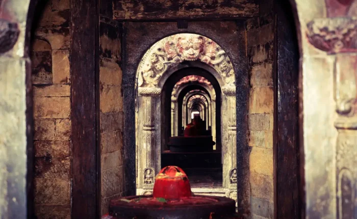 A symmetrical internal view looking through a sequence of stone doorways at a red-painted Shiva Lingam shrine.