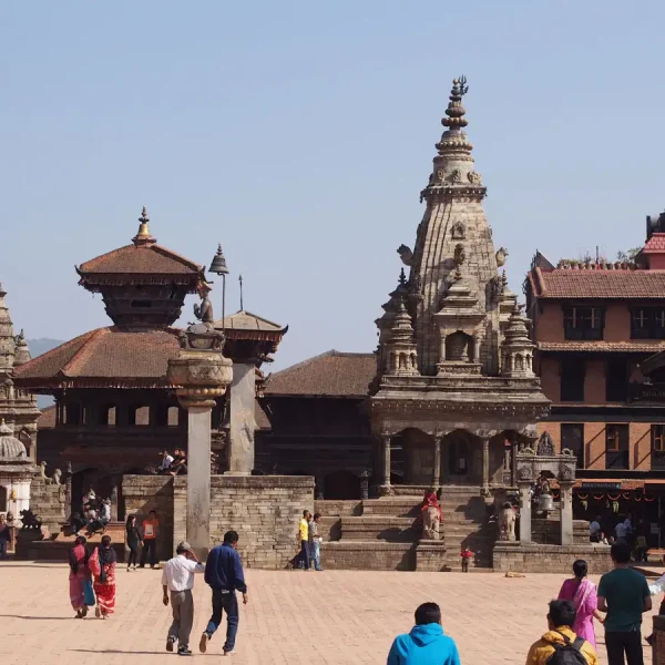 Tourists walking past the stone Siddhi Lakshmi Temple under a clear blue sky during a heritage vacation tour in Bhaktapur.