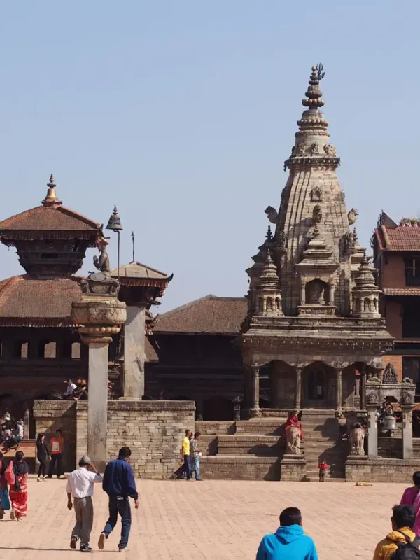 Tourists walking past the stone Siddhi Lakshmi Temple under a clear blue sky during a heritage vacation tour in Bhaktapur.