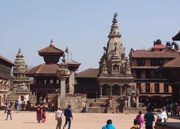 Tourists walking past the stone Siddhi Lakshmi Temple under a clear blue sky during a heritage vacation tour in Bhaktapur.