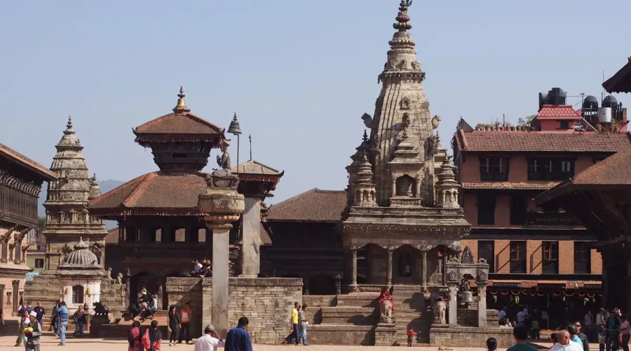Tourists walking past the stone Siddhi Lakshmi Temple under a clear blue sky during a heritage vacation tour in Bhaktapur.