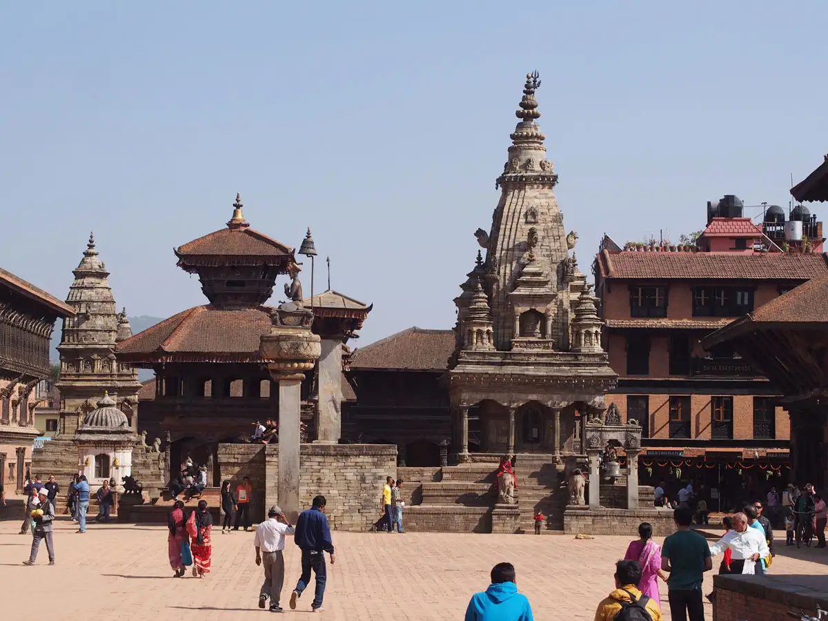Tourists walking past the stone Siddhi Lakshmi Temple under a clear blue sky during a heritage vacation tour in Bhaktapur.