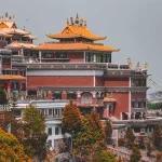 The majestic red and gold tiered architecture of Thrangu Tashi Yangtse Monastery surrounded by autumn trees at Namo Buddha.